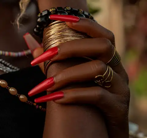 Mãos com unhas compridas e pontiagudas pintadas de vermelho, com pulseiras douradas