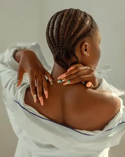 Mulher de costas com cornrows, a pôr a mão no ombro, com as unhas feitas