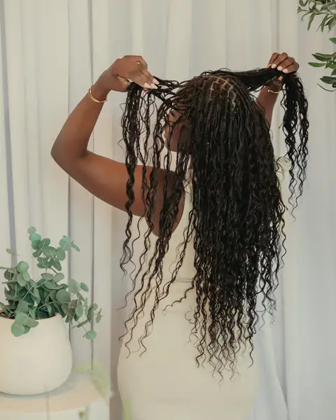Mulher de costas a levantar as tranças compridas, com as pontas encaracoladas
