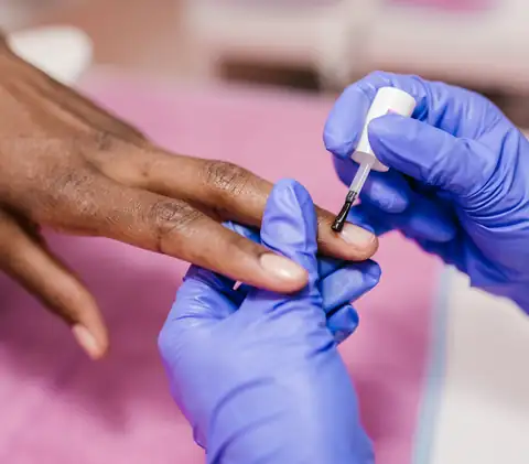 Unhas a serem pintadas numa manicure, com luvas azuis a segurar a mão