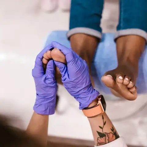 Pés numa cadeira de pedicure, seguros por mãos com luvas lilás