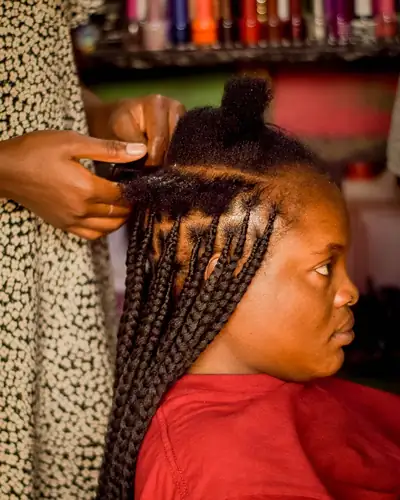 Mãos a fazer tranças no cabelo de uma cliente sentada