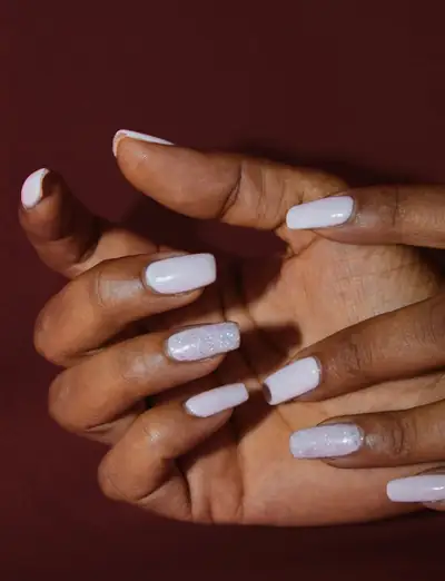 Mãos com unhas pintadas de branco leite sobre um fundo cor de vinho
