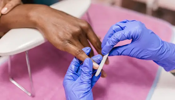 Manicure a arranjar as unhas de uma cliente, com luvas