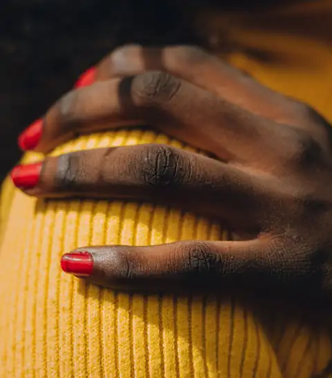 Mão com as unhas pintadas de vermelho, pousada numa camisola amarela